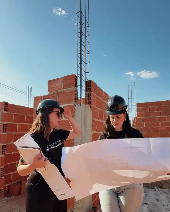 Arquitetas com capacete analisando a planta em um canteiro de obras